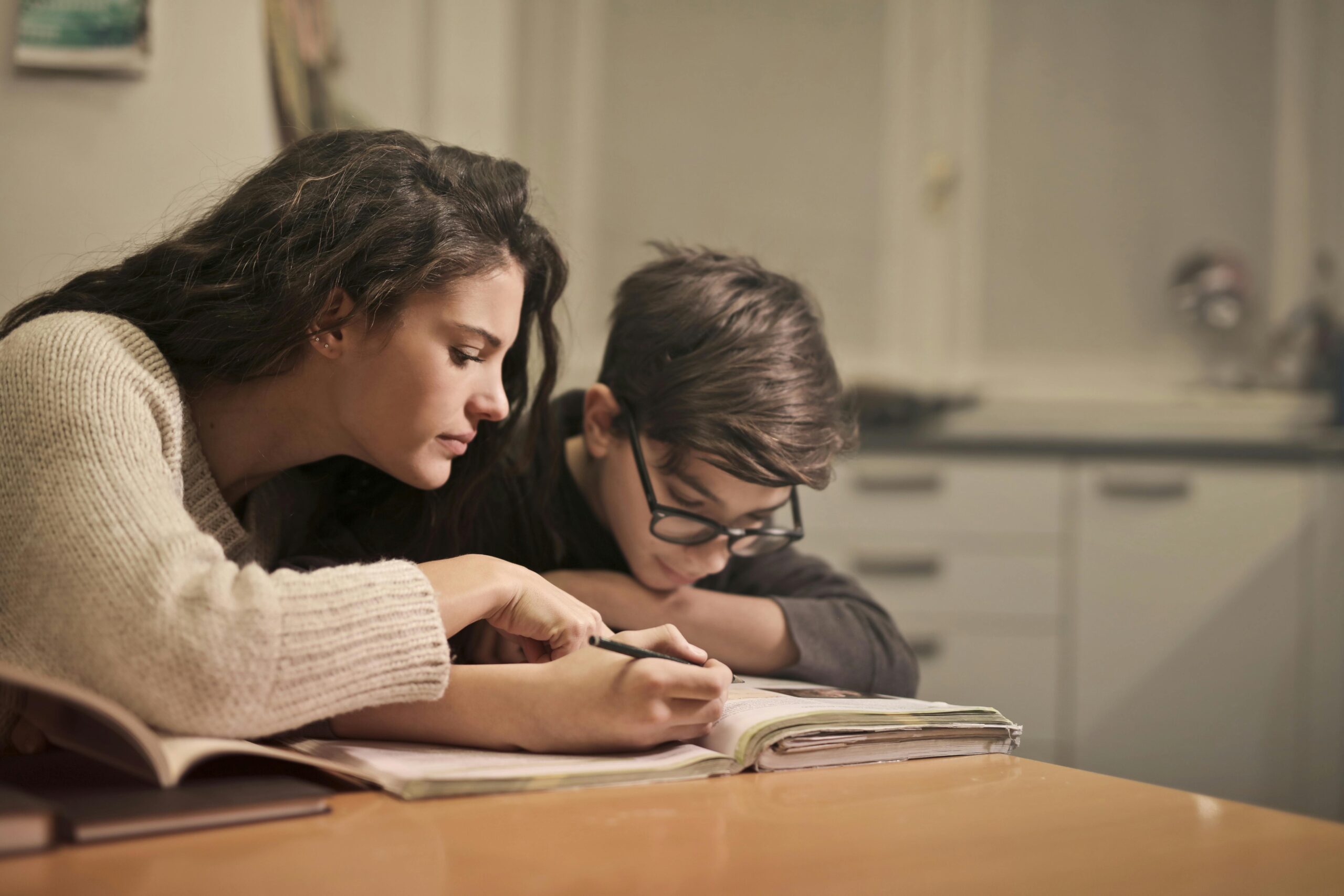 Mum sitting at a table with her son helping him with his reading and writing.