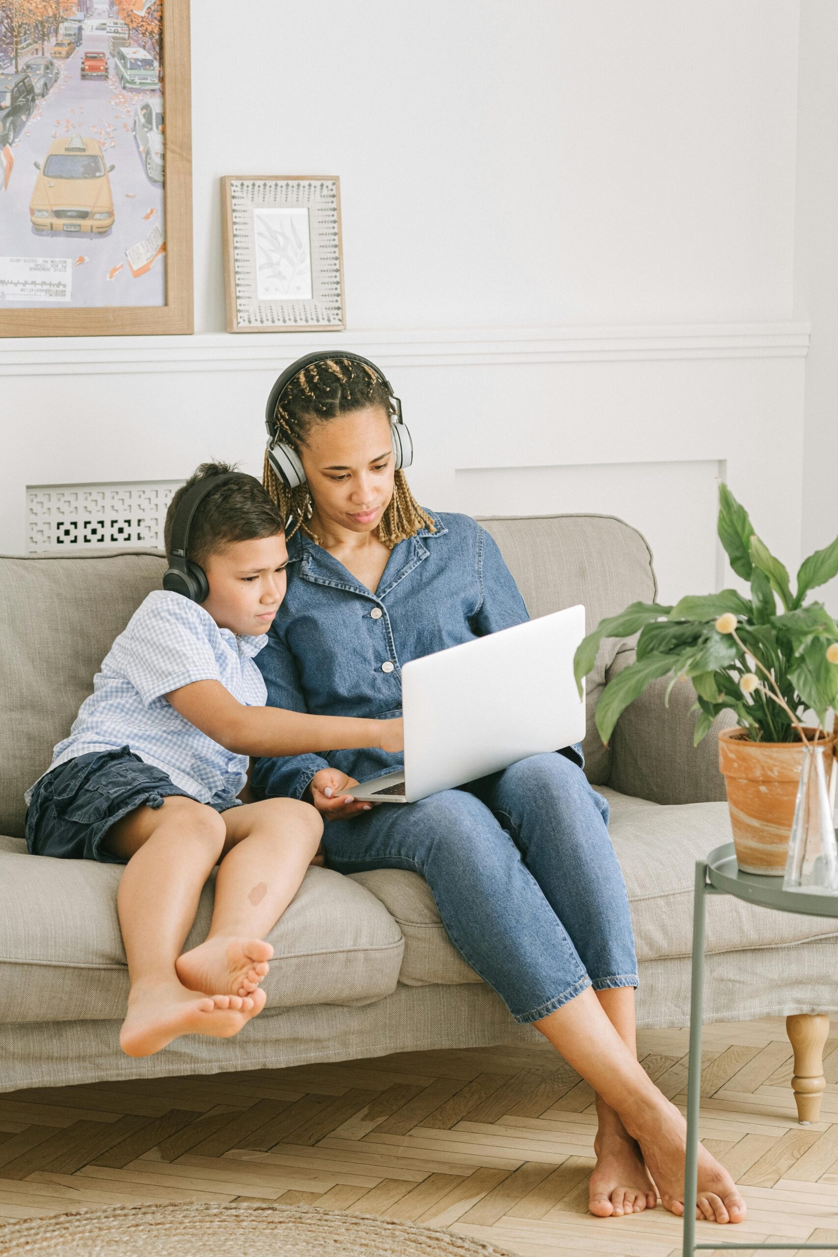 Mum and teen son wearing headphones, sitting on the sofa, watching something on their laptop.