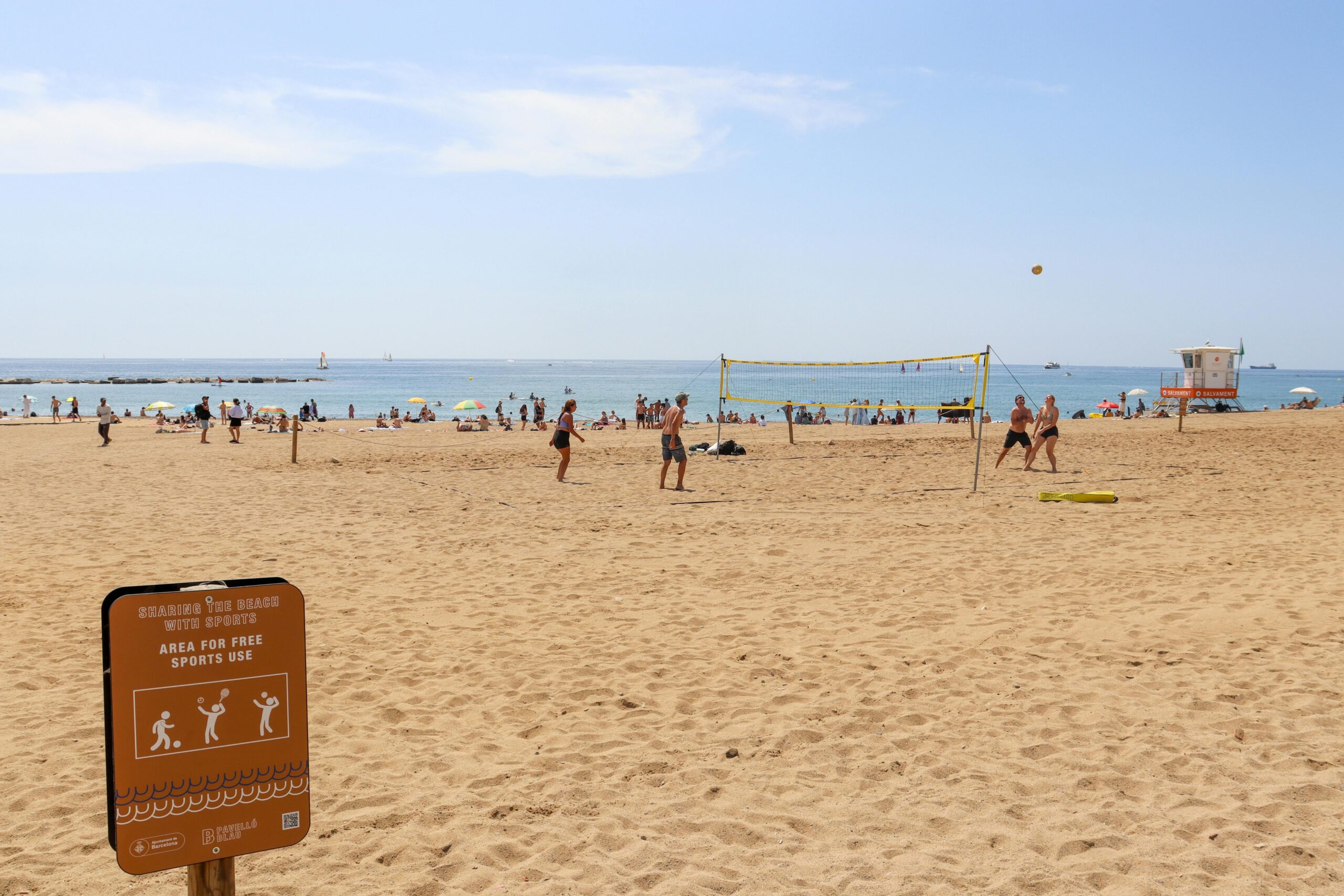 Teens playing at the beach. There is a sign saying 'Sports Playing area'. It is nice sunny day with blue skies.